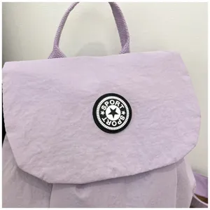 Vue détaillée du mini sac à dos décontracté violet avec écusson sport rond et poignée.