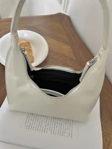Primo piano sui dettagli della borsa a spalla a mezzaluna in vernice crema con zip.