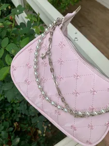 Pink quilted baguette bag detail, featuring embroidered bows, pearls and metal chain decoration.