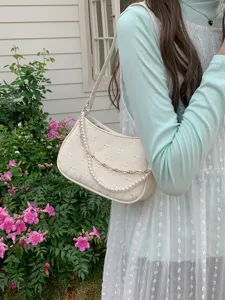 Quilted baguette shoulder bag detail featuring elegant bow patterns, pearl and chain strap.