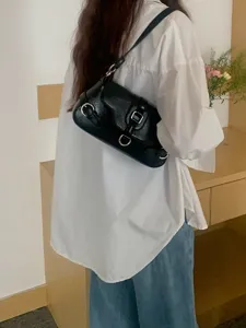Detail view of women black motorcycle style underarm shoulder bag with metal rings and strap.