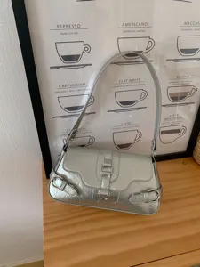 Silver metallic shoulder bag detail showing glossy PU leather finish and stylish metal buckles.