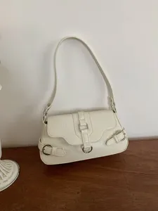 Detail shot of a chic white underarm shoulder bag with metal buckle and motorcycle style.