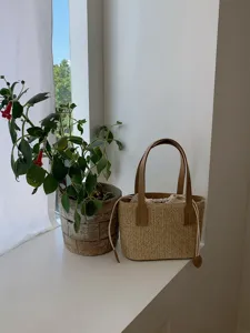 Close-up view of woven straw bucket bag detail with brown leather handles and interior lining.