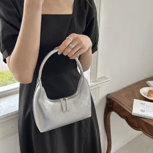 Dettaglio della borsa a mezzaluna argentata con finitura in pelle metallizzata e chiusura a zip.
