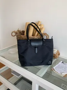 Detailed view of a classic black nylon tote bag featuring a leather flap on a glass table.