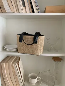 Close-up view of a stylish straw woven handbag displayed on a white shelf in a room setting.