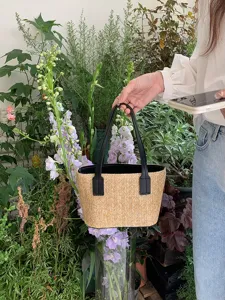 Detailed view of the summer straw woven bucket bag in a natural plant scene setting.
