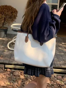 Detailed view of white minimalist commuter tote bag with contrast brown shoulder straps.
