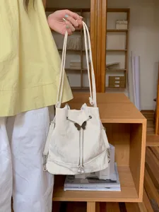 Stylish white bucket bag with cute butterfly metal drawstring detail for daily fashion use.