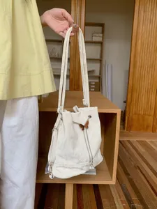Detailed view of white bucket backpack with butterfly charm and pearl pendant versatile style.