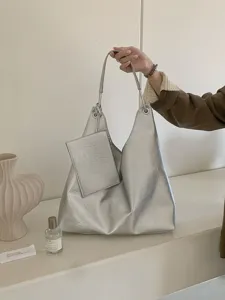 Detailed view of silver shoulder hobo bag with small pouch in minimalist indoor setting scene.