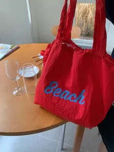 Gedetailleerd overzicht van de rode nylon tote tas met blauwe Beach print en handig koord.