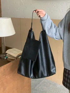 Detail shot of a casual black PU leather tote bag with a small attached pouch in hand.