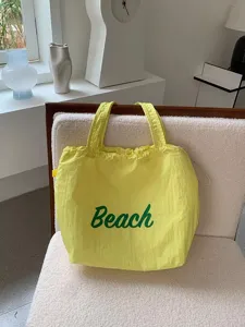 Close-updetail van de gele canvas tote tas met groene strandtekst en handig aantrekkoord.