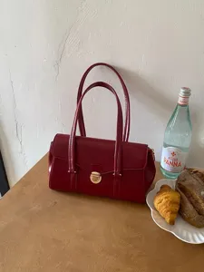 Red leather top handle bag detail shot on wooden table with elegant lifestyle setting.