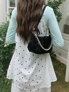 Detail view of black crinkled baguette shoulder bag with pearl and metal chain straps.