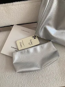 Detail view of a stylish silver metallic tote bag and matching pouch on fluffy white setup.