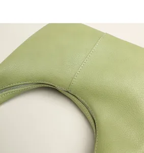 Detailed view of the green leather underarm bag showing fine texture and zipper.