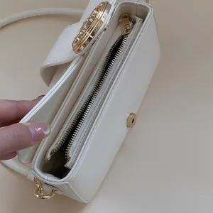 White shoulder bag detail view showing smooth zipper closure and premium gold hardware.