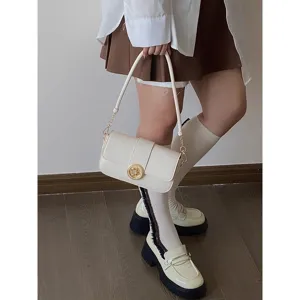 Close-up detail of stylish white shoulder bag featuring elegant gold round clasp and strap.