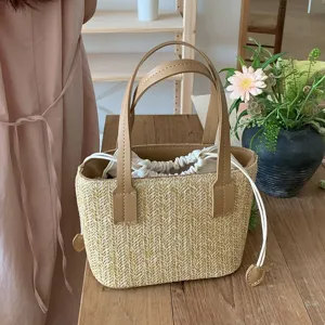 Summer straw woven bucket bag with leather handles and drawstring closure for beach vacation.