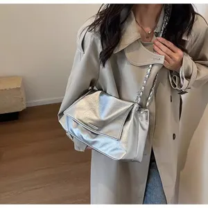 Detail shot of a silver metallic shoulder bag with chain strap worn by model in trench coat.