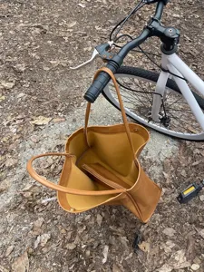 Detail view of brown soft leather tote bag hanging on bicycle outdoors with pouch inside.