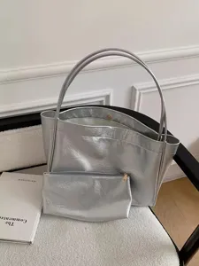 Close-up of a silver metallic tote bag with matching pouch on a plush cushion setting.