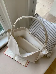 Detailed view of the elegant beige minimalist leather tote bag with inner pouch on soft cushion.