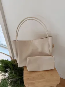 Minimalist beige PU leather tote bag and pouch detail in a warm cozy indoor setting.