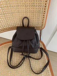 Dark brown mini leather backpack detail, featuring flap closure and slender shoulder straps.