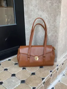 Close-up detail of retro brown leather shoulder tote bag, classic lock closure and dual straps.