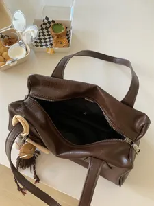 Detailed shot of dark brown retro leather underarm bag with cute sports pendant and soft texture.