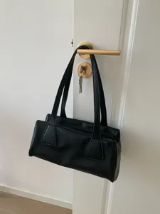 Detail view of black vintage baguette shoulder bag hanging on handle, minimalist style.