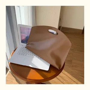 Detail shot of a brown leather 13-inch laptop sleeve placed on a white desk setup.
