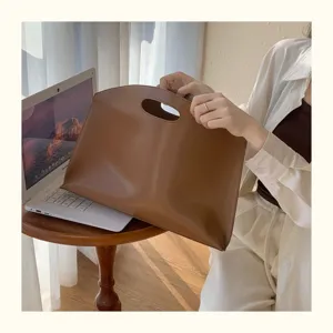 Detail shot of brown leather laptop bag with cutout handle in cozy indoor setting for office commute.