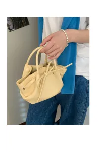 Borsa a mano da donna giallo chiaro a secchiello con fiocco, dettaglio accessorio moda primavera estate.