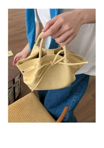 Primo piano del borsetto secchiello in pelle gialla con elegante fiocco e pratici manici.
