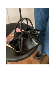 Vista dettagliata di una borsa a secchiello nera lucida con fiocco, borsa chic da donna.