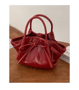 Dettaglio in primo piano della borsa a mano in pelle verniciata rossa con fiocco e manici.
