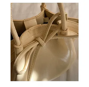 Primo piano dettagliato di una borsa a secchiello beige crema con elegante fiocco e manico.