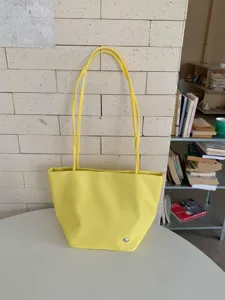 Detail view of a stylish yellow tote bag with slim shoulder straps on a clean white table.