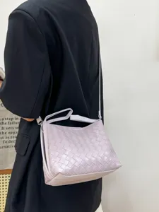 Detail view of a chic purple woven leather shoulder bag worn with a black blazer.