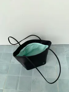 Close-up detail of a black nylon tote bag with mint green inner lining and long shoulder straps.