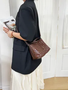 Detailed shot of a dark brown woven leather shoulder crossbody bag worn by a model in a blazer.
