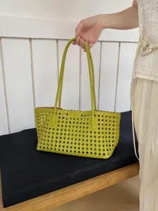Green woven tote bag detail showing intricate cutout lattice leather design and dual handles.