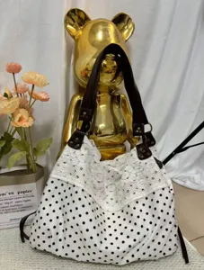 Detailed view of polka dot canvas shoulder bag with delicate white lace trim and dark straps.