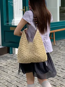 Detail view of summer straw woven shoulder bag, hollow design beach tote with wooden bead handle.