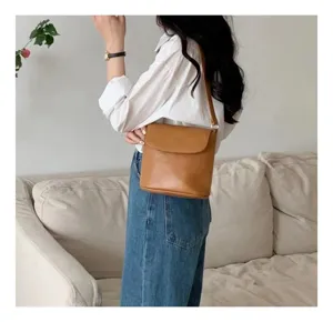 Detail view of a stylish brown leather bucket bag worn by model on shoulder indoors scene.